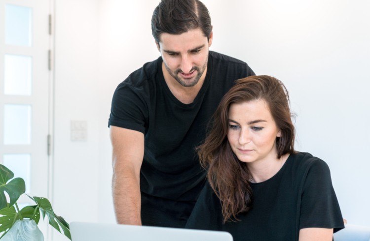 Liam Austin and Sarah Thorslund are seen coaching clients online, both focused on a laptop screen while collaborating in a minimalist workspace.