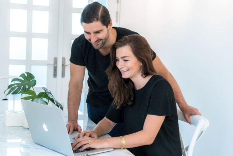 Liam Austin and Sarah Thorslund working together on a laptop, smiling as they collaborate to help clients achieve their goals.