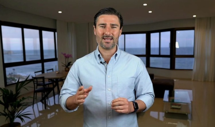 Liam Austin standing in a bright room with ocean views, speaking on camera to give advice about coaching and consulting.