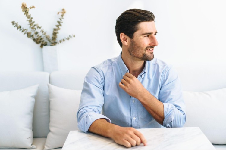 Man sitting at a table adjusting his shirt collar, looking thoughtful as if reflecting on setting goals.