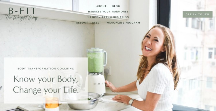 Smiling body transformation coach preparing a healthy smoothie in a bright kitchen to help clients enhance their well-being.